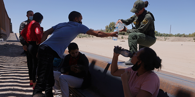 U.S. Border Patrol officer gives water to detained migrants waiting to be transported by the U.S. Border Patrol after crossing into the United States from Mexico in Andrade, California, U.S., April 19, 2021.