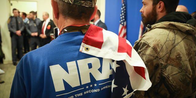 man in blue NRA shirt with US flag draped on shoulder