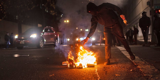 A protester feeds a small fire near the south entrance of the Justice Center after a riot was declared during a protest to decry the verdict in the Kyle Rittenhouse Trial. Portland, Oregon, USA, November 19th, 2021.