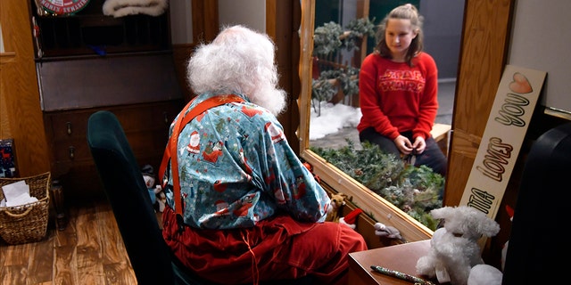 Santa, Sid Fletcher, sits behind glass as he gets a Christmas wish list from Kendra Alexander of St. James, Minnesota, during her visit Monday, Nov. 15, 2021, at the Mall of America in Bloomington, Minnesota.