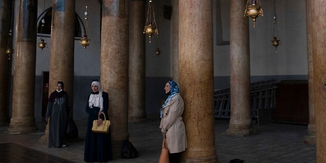 Tourists pose for a photo with renovated polished limestone columns, during a visit to the Church of the Nativity, in the West Bank city of Bethlehem, Tuesday, Nov. 16, 2021.