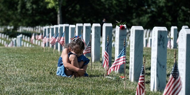 A girl reacts in front of a headstone during Memorial Day as visitors honor veterans and those lost in war at Arlington National Cemetery in Virginia on May 31, 2021.  