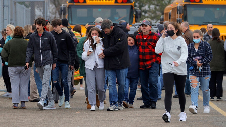Parents walk away with their kids from the Meijer's parking lot in Oxford where many students gathered following an active shooter situation at Oxford High School in Oxford on November 30, 2021.