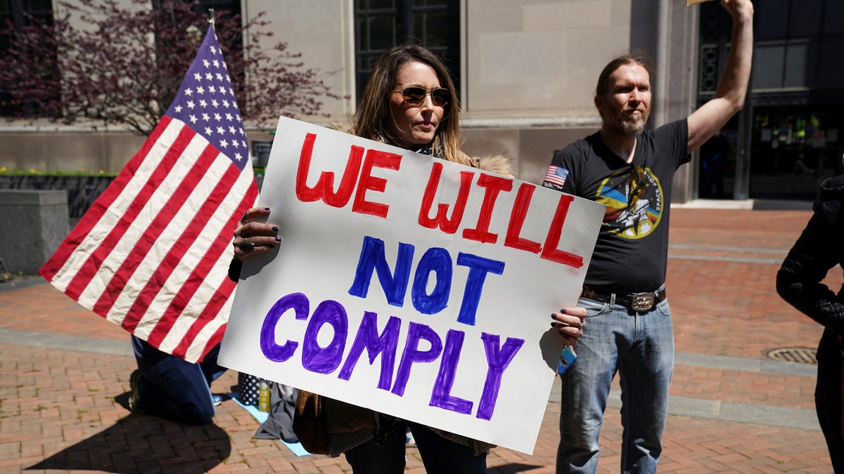 A protestor carries a sign reading "We Will Not Comply" during a demonstration outside the Virginia State Capitol to protest Virginia's stay-at-home order and business closures in the wake of the coronavirus disease (COVID-19) outbreak in Richmond, Virginia, U.S., April 16, 2020. 