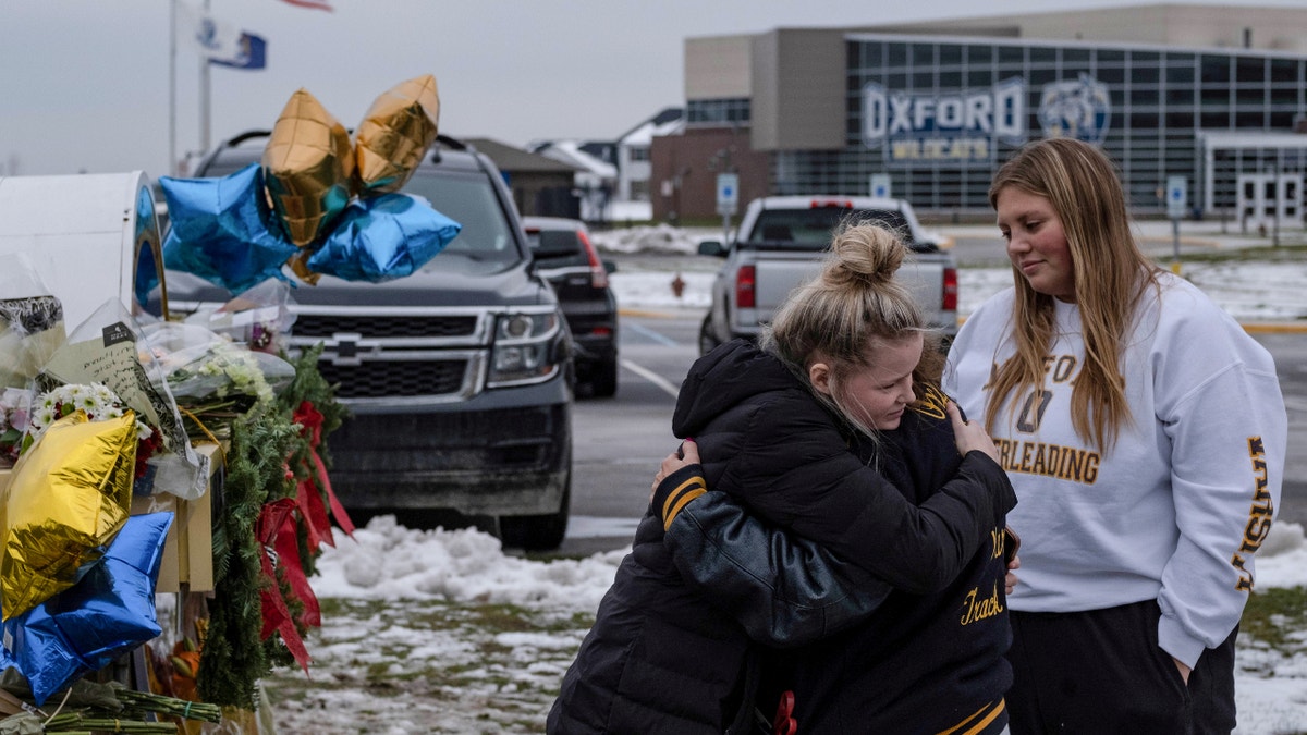 People embrace as they pay their respects at a memorial at Oxford High School, a day after a shooting