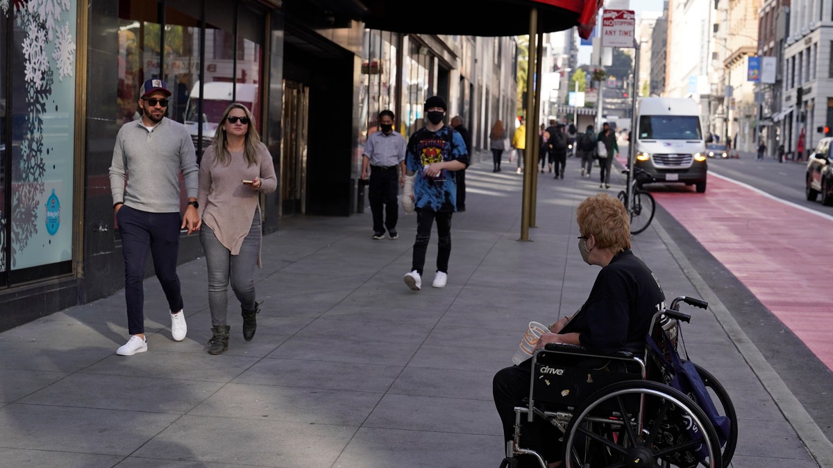 People pass by a woman in a wheelchair panhandling near Union Square in San Francisco, Thursday, Dec. 2, 2021. (AP Photo/Eric Risberg)