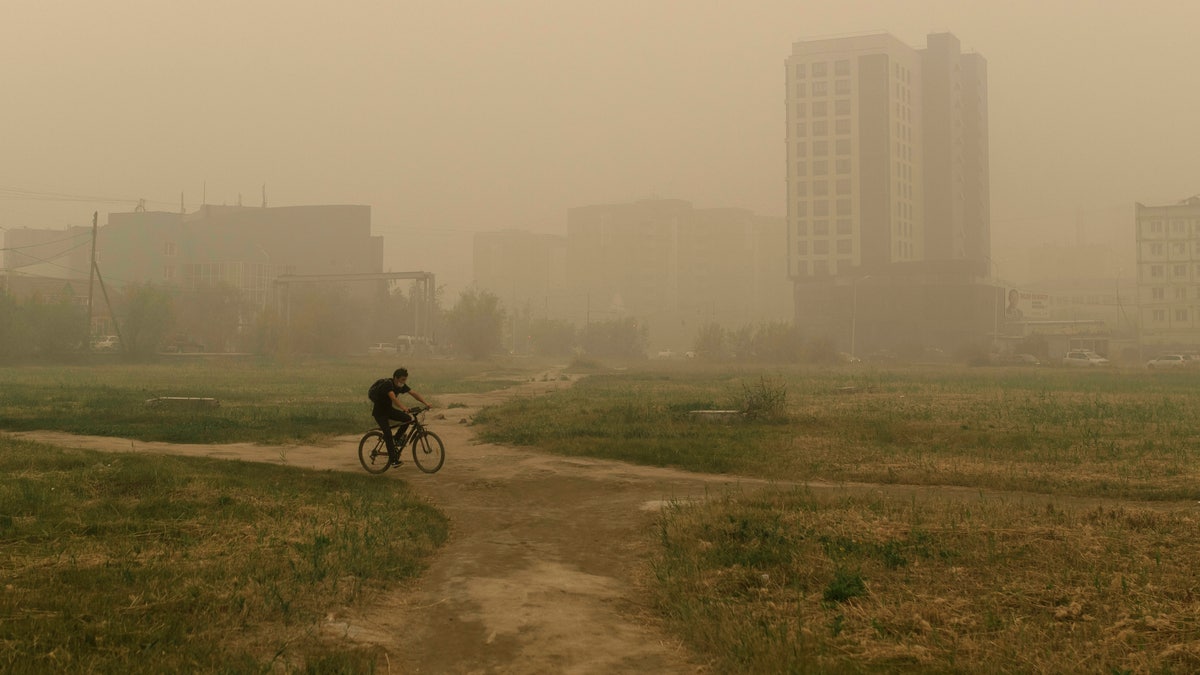 A man rides his bicycle through smoke from a forest fire covers Yakutsk, the capital of the republic of Sakha also known as Yakutia, Russia Far East, Russia, Thursday, Aug. 12, 2021. (AP Photo/Ivan Nikiforov, File)