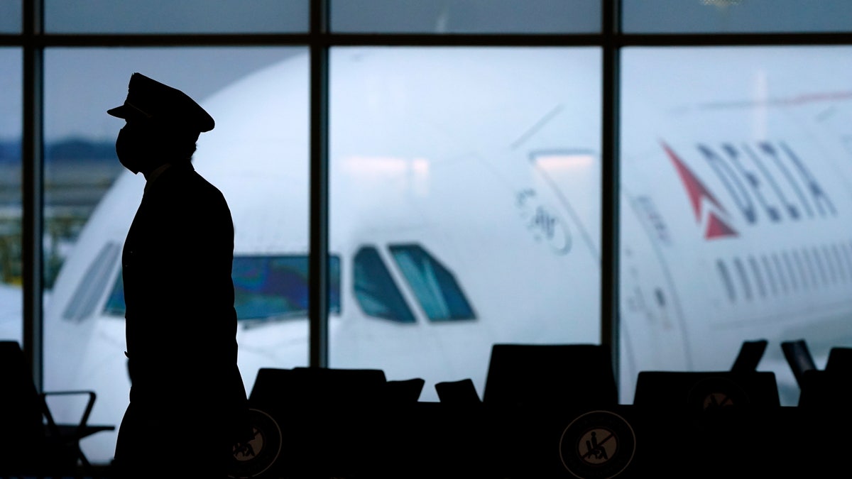 FILE - A Delta Airlines pilot wears a face mask as he walks through a terminal at Hartsfield-Jackson International Airport in Atlanta.