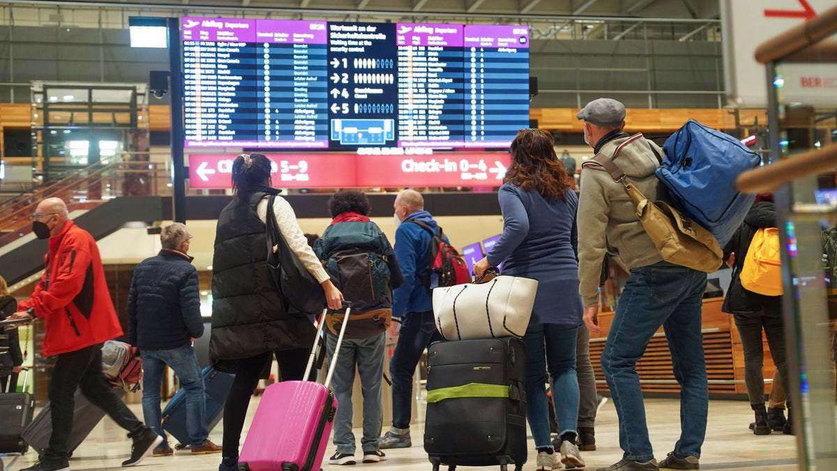 Travellers stand in front of an information board at BER Airport in Berlin, Germany, Saturday, Dec. 18, 2021. Germany’s incoming transport minister is advising people against traveling over Christmas as the country tries to stem a wave of coronavirus infections. (Joerg Carstensen/dpa via AP)