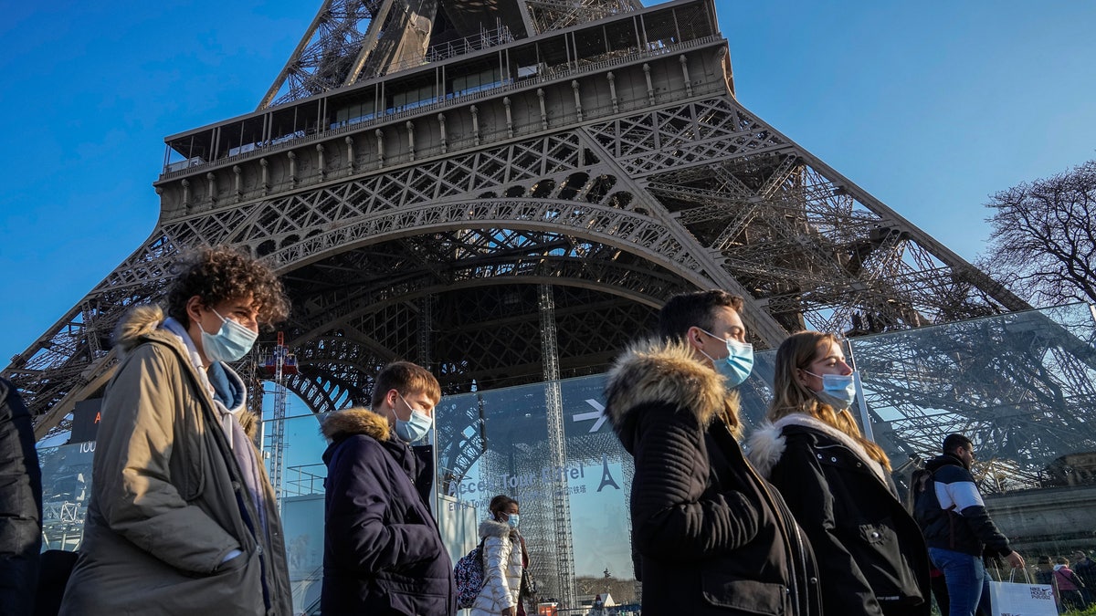 People wearing face masks to protect against COVID-19 walk past the Eiffel Tower in Paris, Tuesday, Dec. 21, 2021.(AP Photo/Michel Euler)