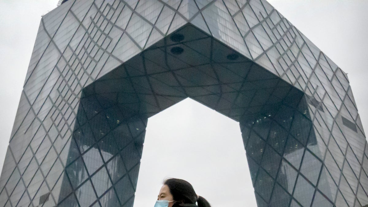 A woman wearing a face mask to protect against COVID-19 walks along a street in the central business district in Beijing, Thursday, Dec. 23, 2021. (AP Photo/Mark Schiefelbein)