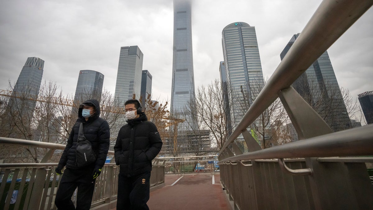 Commuters wearing face masks to protect against COVID-19 walk across a pedestrian bridge in the central business district in Beijing, Thursday, Dec. 23, 2021. (AP Photo/Mark Schiefelbein)