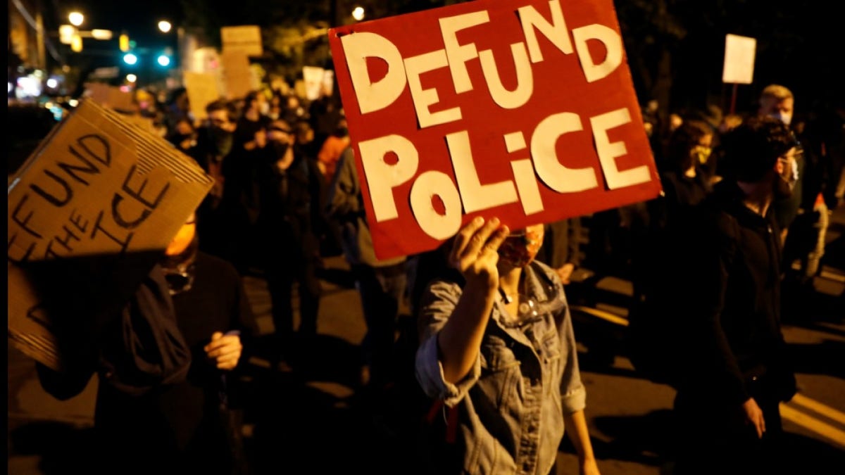 protesters hold "Defund the Police" signs