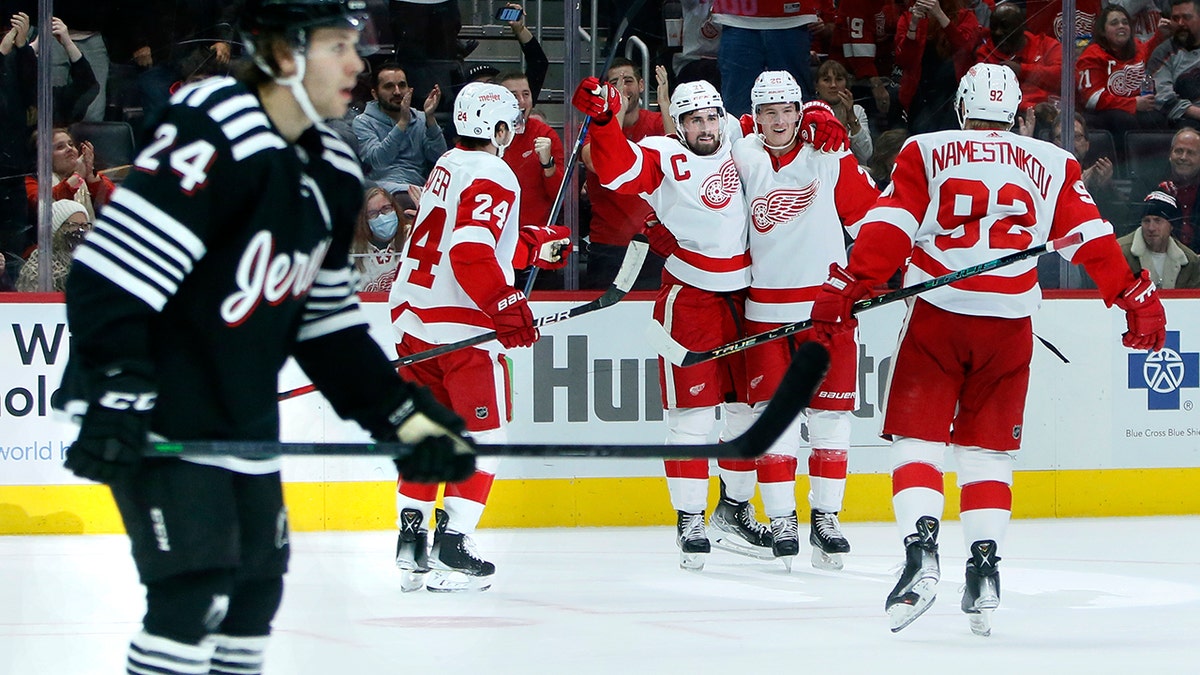 Detroit Red Wings center Dylan Larkin, third from left, celebrates his second goal of the game with center Pius Suter (24), defenseman Gustav Lindstrom and center Vladislav Namestnikov (92) as New Jersey Devils defenseman Ty Smith (24) skates off during the second period of an NHL hockey game Saturday, Dec. 18, 2021, in Detroit.