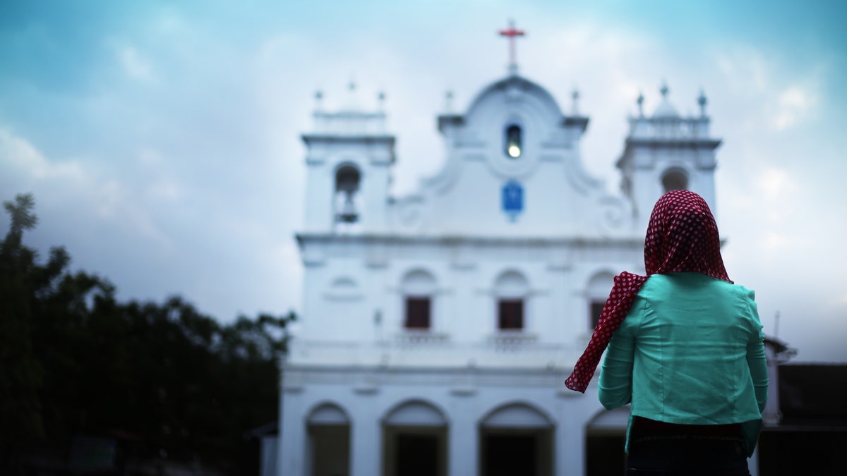 Young Christian woman standing in front of a church in Goa, India. (rvimages via Getty Images)