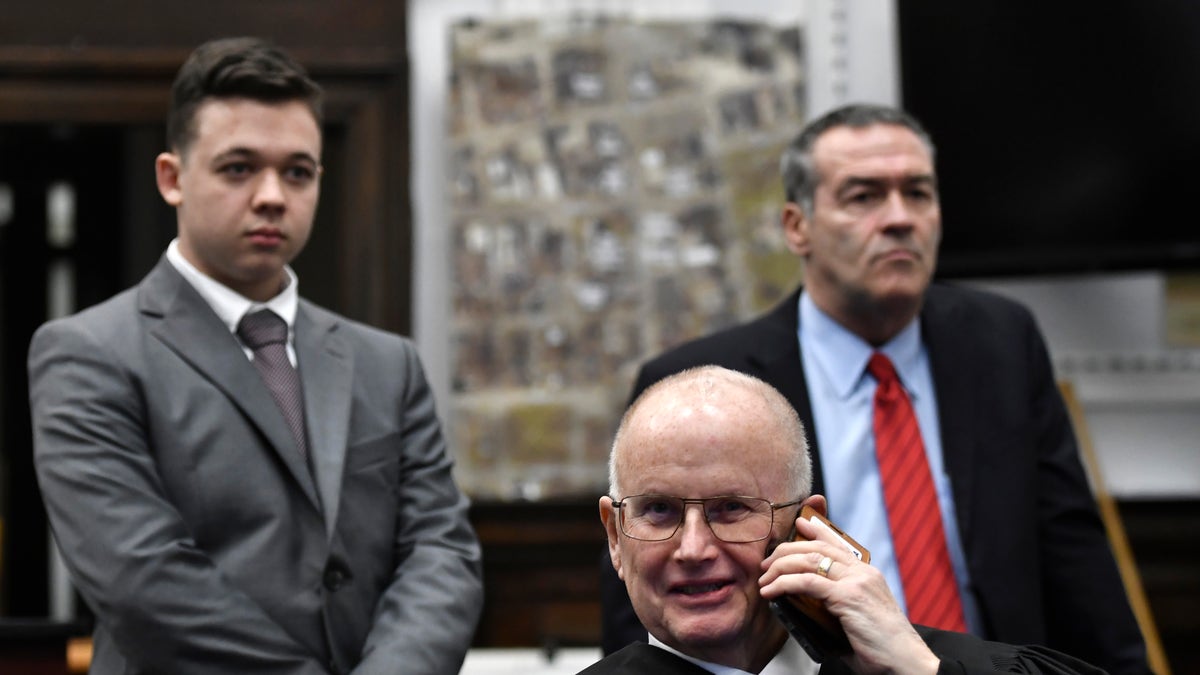 Judge Bruce Schroeder takes a personal call as the court waits for an evidence video to be played. Kyle Rittenhouse, left, and his attorney Mark Richards stand behind the judge at the Kenosha County Courthouse Nov. 12, 2021 in Kenosha, Wis. 