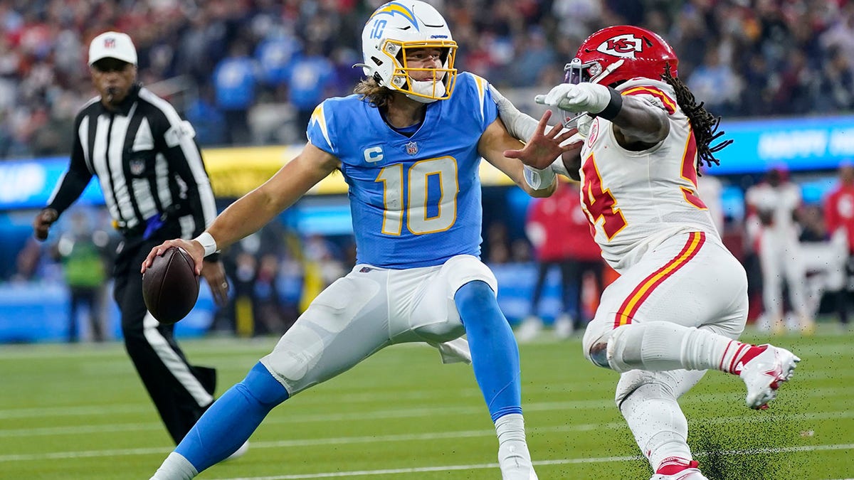 Los Angeles Chargers quarterback Justin Herbert, left, looks to pass under pressure from Kansas City Chiefs outside linebacker Nick Bolton during the second half of an NFL football game Thursday, Dec. 16, 2021, in Inglewood, California.