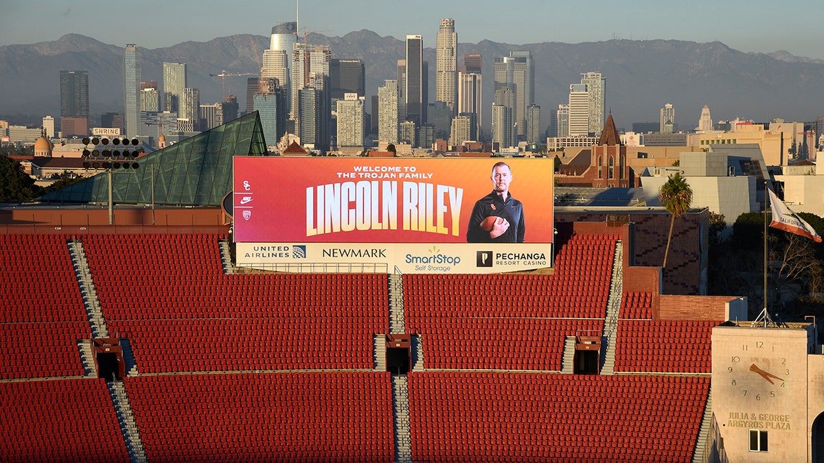 A large billboard at the Los Angeles Coliseum displays a photo of new USC football coach Lincoln Riley with downtown Los Angeles as a backdrop.