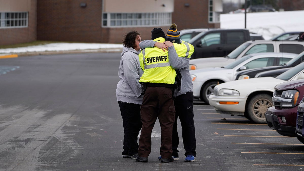 An Oakland County Sheriff's deputy hugs family members of a student in the parking lot of Oxford High School in Oxford, Mich., Wednesday, Dec. 1, 2021. A 15-year-old sophomore opened fire at the school, killing several students and wounding multiple other people, including a teacher. (AP Photo/Paul Sancya)