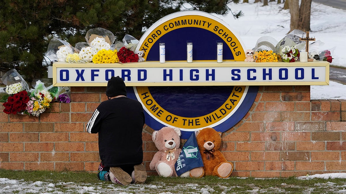 A well wisher kneels to pray at a memorial on the sign of Oxford High School in Oxford, Mich., on Wednesday, Dec. 1, 2021. A 15-year-old sophomore opened fire at the school, killing several students and wounding multiple other people, including a teacher. (AP Photo/Paul Sancya)