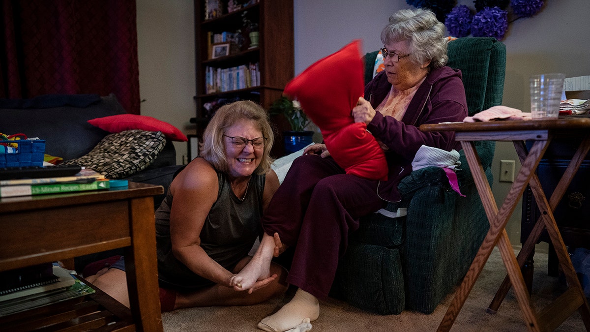 Susan Ryder, 54, giggles as she applies an ointment to the base of her mother's foot before bedtime, Monday, Nov. 29, 2021, in Rotterdam Junction, New York.