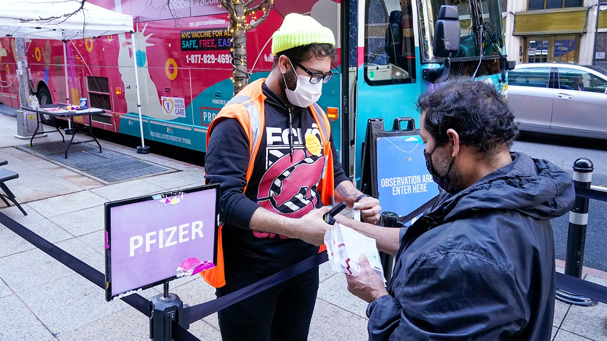 A health care worker, left, checks in a man at a NYC mobile vaccine clinic