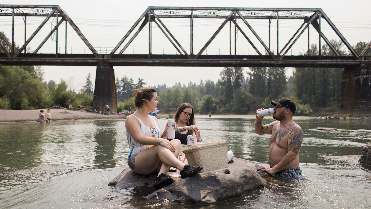 Mirian Perala, Addie Cold and Joe St. Martin enjoy lunch on a rock in the middle of the Sandy River near Troutdale, Oregon, Aug.13 during a heat wave. 