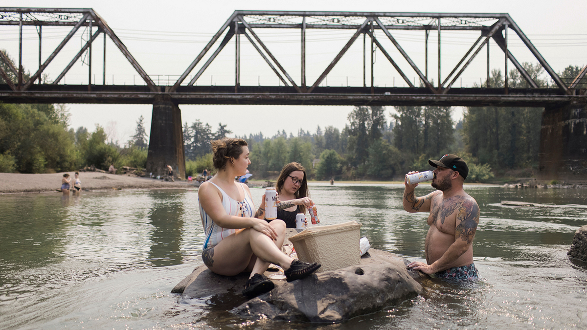 Mirian Perala, Addie Cold and Joe St. Martin enjoy lunch on a rock in the middle of the Sandy River near Troutdale, Oregon, Aug.13 during a heat wave.