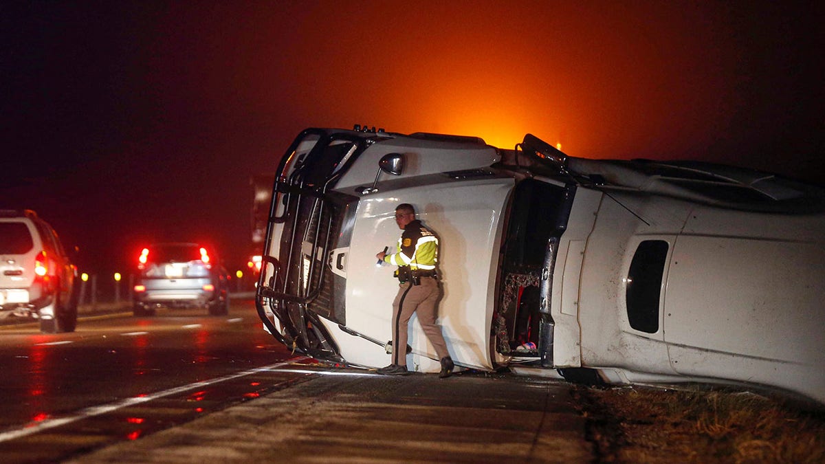 An Iowa State Patrol trooper works the scene of an overturned semi-truck along the westbound shoulder of Interstate 80 near Anita, Iowa, after a band of intense weather crossed through the area. 