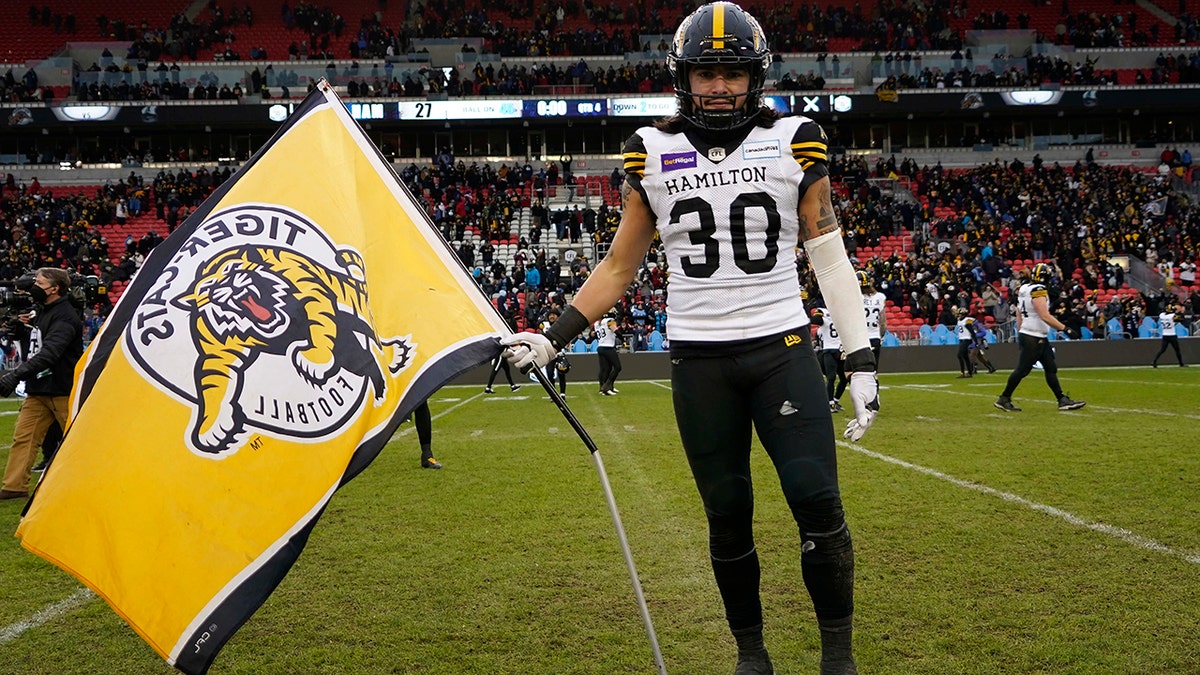 Dec 5, 2021; Toronto, Ontario, CAN; Hamilton Tiger-Cats defensive back Stavros Katsantonis (30) poses with a team flag on the field after a win over the Toronto Argonauts in the Canadian Football League Eastern Conference Final game at BMO Field.