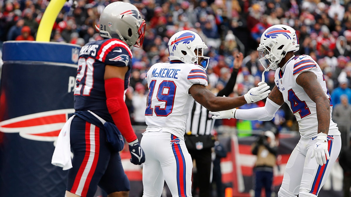 Buffalo Bills wide receiver Isaiah McKenzie (19) is congratulated by Stefon Diggs (14) after his touchdown during the first half of an NFL football game, Sunday, Dec. 26, 2021, in Foxborough, Massachusetts. At left is New England Patriots safety Adrian Phillips (21).