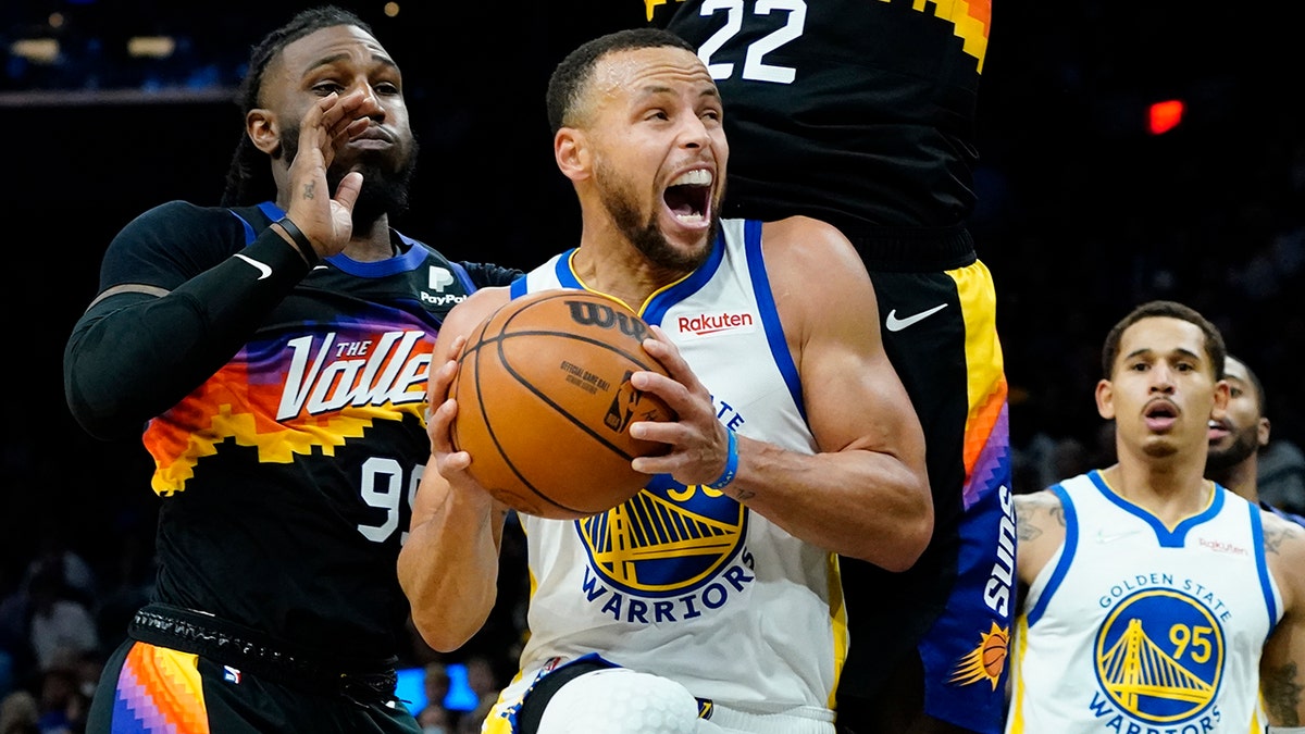 Golden State Warriors guard Stephen Curry drives past Phoenix Suns forward Jae Crowder, left, and center Deandre Ayton (22) during the first half of an NBA basketball game, Tuesday, Nov. 30, 2021, in Phoenix.