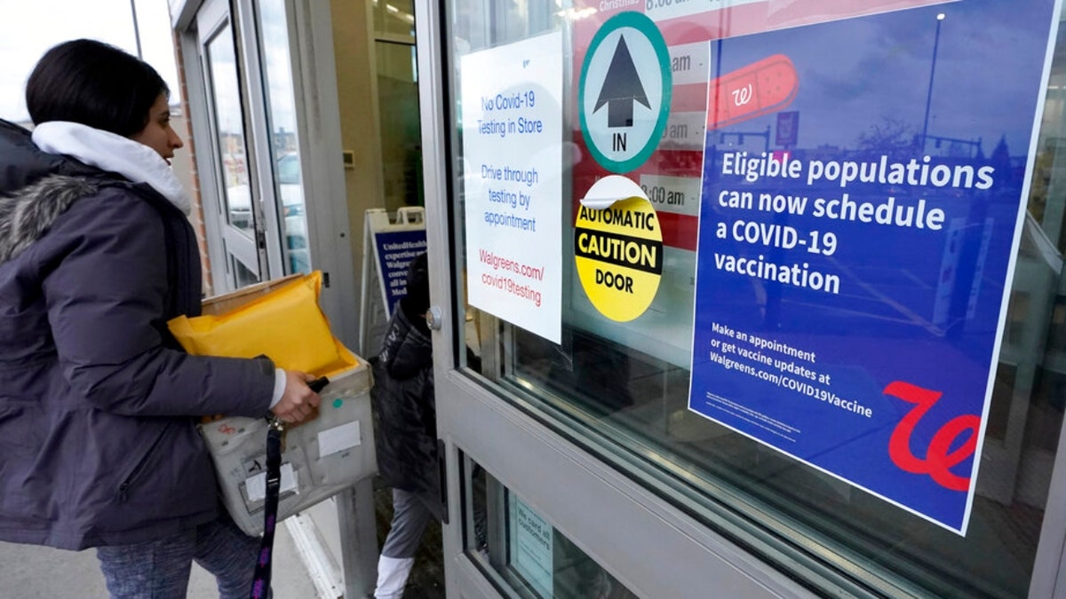 A passer-by enters a pharmacy with a vaccination advisory attached to a door, right, Thursday, Dec. 2, 2021, in Worcester, Mass. As the U.S. recorded its first confirmed case of the omicron variant, doctors across the country are experiencing a more imminent crisis with a delta variant that is sending record numbers of people to the hospital in New England and the Midwest. (AP Photo/Steven Senne)