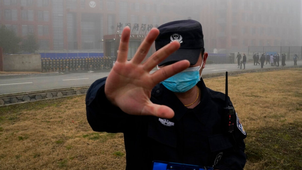 A security person moves journalists away from the Wuhan Institute of Virology.