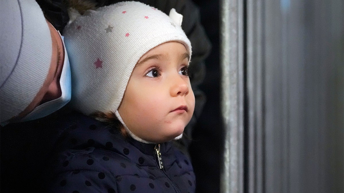 A baby looks at a stand where a person wearing a Santa Claus outfit greets children at a Christmas fair in Bucharest, Romania, Friday, Dec. 17, 2021.