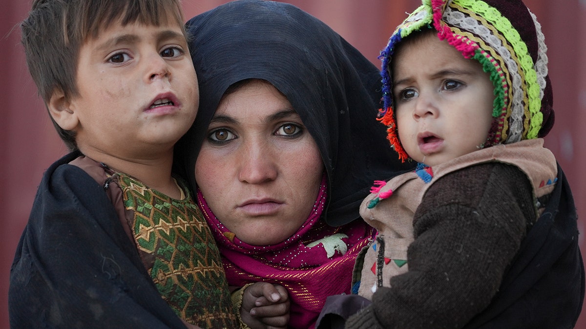 An Afghan woman holds her children as she waits for a consultation outside a makeshift clinic at a sprawling settlement of mud brick huts housing those displaced by war and drought near Herat, Afghanistan, Dec. 16, 2021.