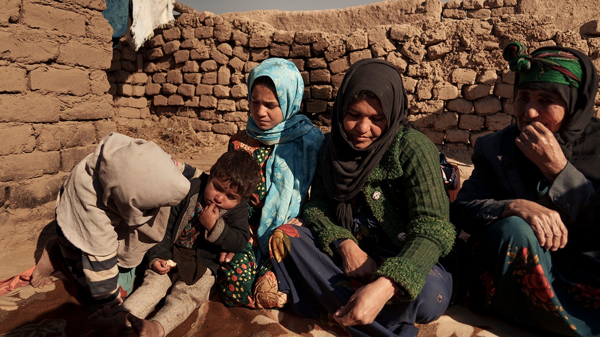 Aziz Gul, second from right, and her 10-year-old daughter Qandi, center, sit outside their home with other family members, near Herat, Afghanistan, Dec. 16, 2021.