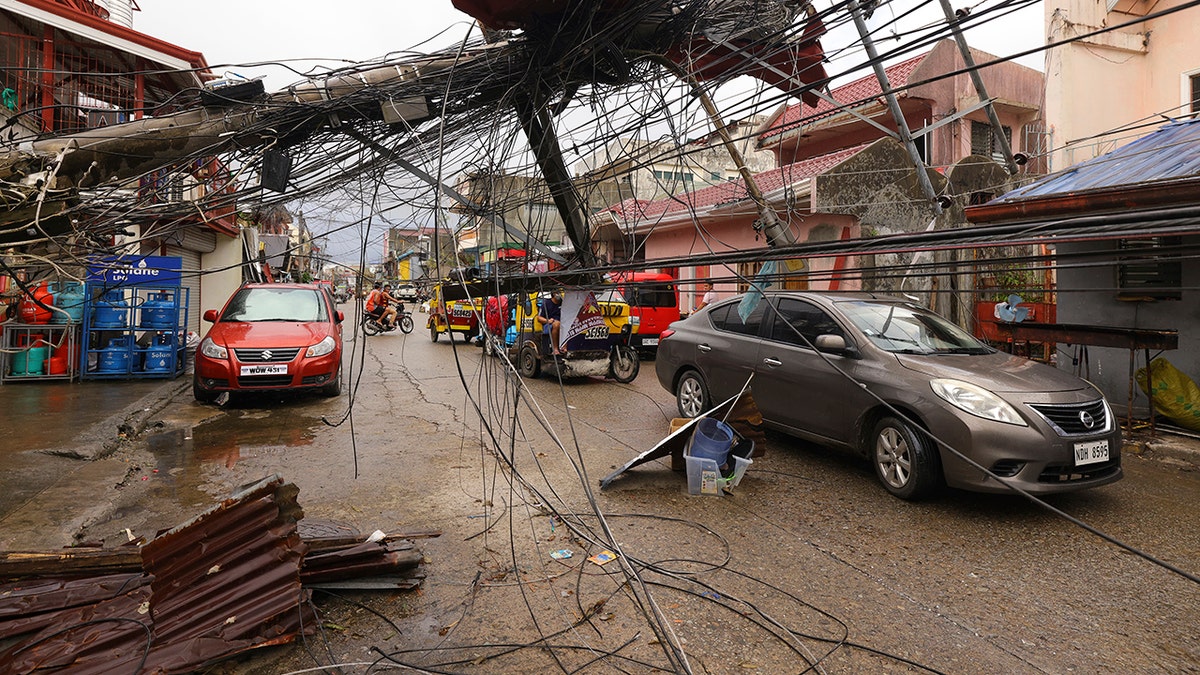  cars pass by a toppled electrical post due to Typhoon Rai in Surigao city, Surigao del Norte, southern Philippines as power supply remain down on Sunday Dec. 19, 2021. 