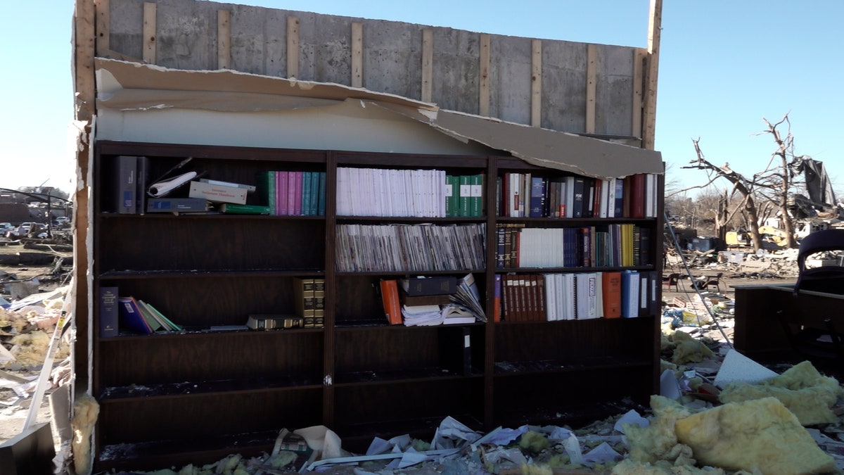 A bookcase left standing amidst rubble in Mayfield