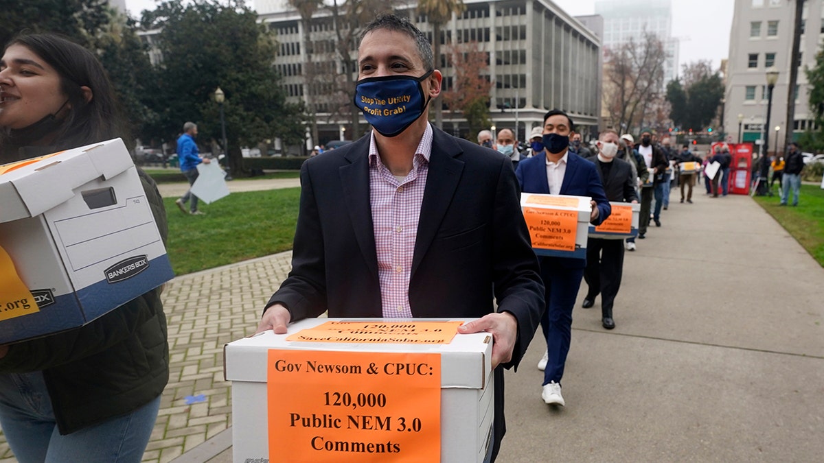 Solar energy advocates carry boxes of petitions against proposed reforms that they claim would handicap the rooftop solar market to the governor's office at the Capitol in Sacramento, California, Wednesday, Dec. 8, 2021.