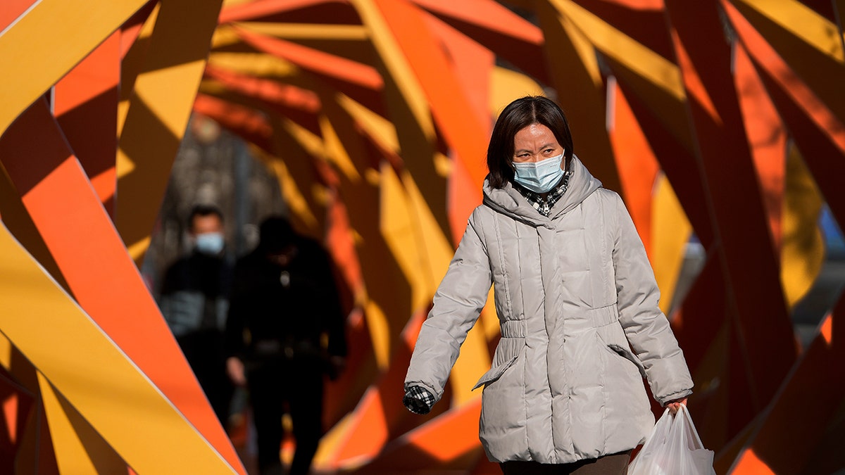 A woman wearing a face mask to help protect from the coronavirus looks as she walks by an art installation depicting a prosperity chamber on display outside a mall in Beijing, Monday, Dec. 27, 2021. 
