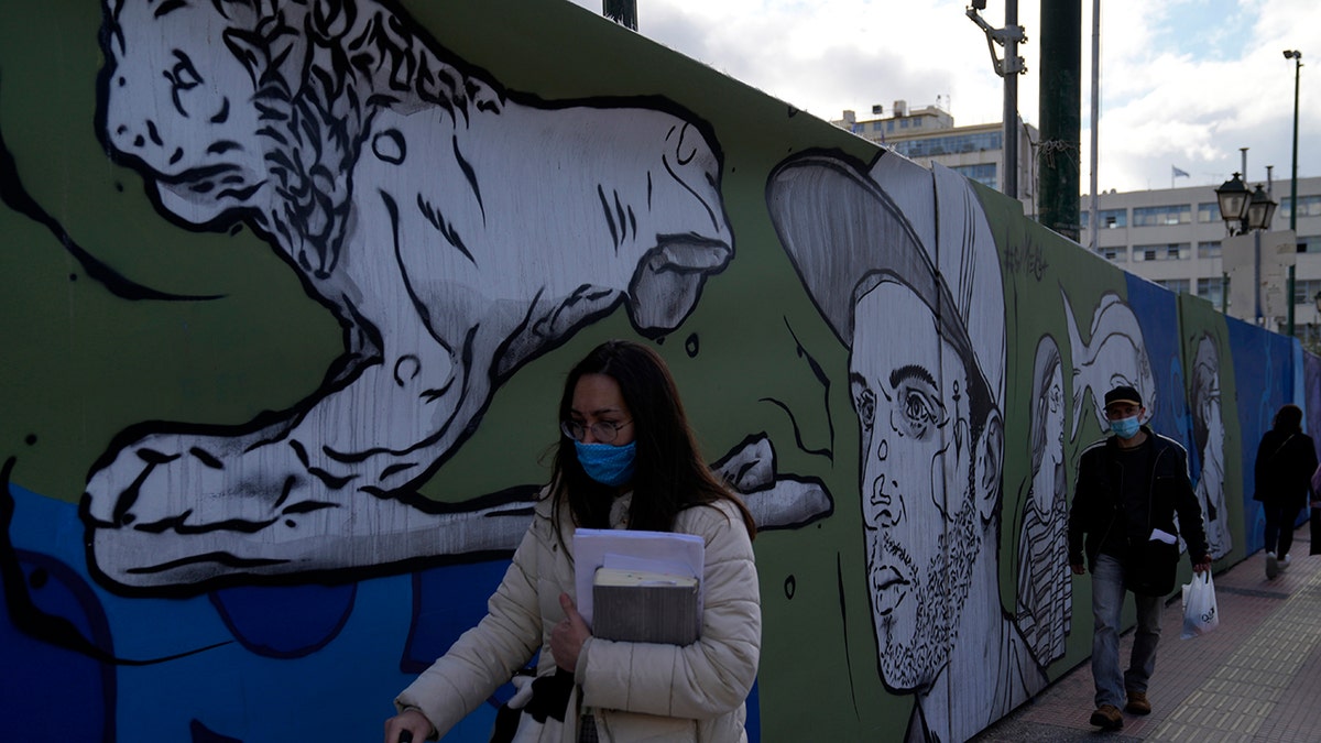 People wearing face masks to protect against COVID-19 walk at the port of Piraeus, near Athens, Greece, Monday, Dec. 13, 2021.