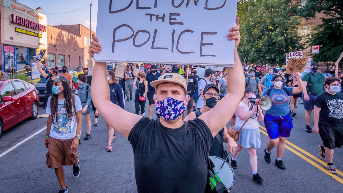 A masked demonstrator in New York holds a "defund the police" sign