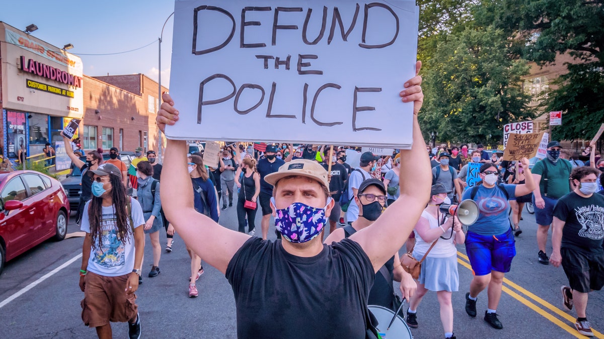 A masked demonstrator in New York holds a "defund the police" sign