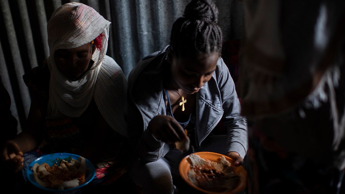 Displaced Tigrayan women, one wearing an Ethiopian Orthodox Christian cross, sit in a metal shack to eat food donated by local residents at a reception center for the internally displaced in Mekele, in the Tigray region of northern Ethiopia, on May 9, 2021. 