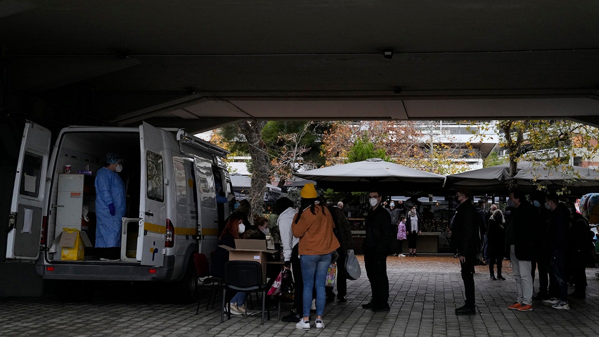 A member of the medical staff at the National Public Health Organisation (EODY) conducts a COVID-19 rapid test on a woman as others wait in a queue in Athens, Greece, Wednesday, Dec. 29, 2021.