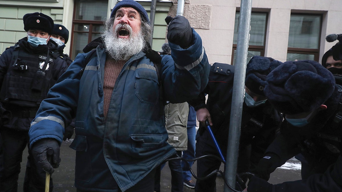 Police officers unlock a man who chained himself to a pole in front of the Supreme Court of the Russian Federation in Moscow, Russia, Tuesday, Dec. 28, 2021.