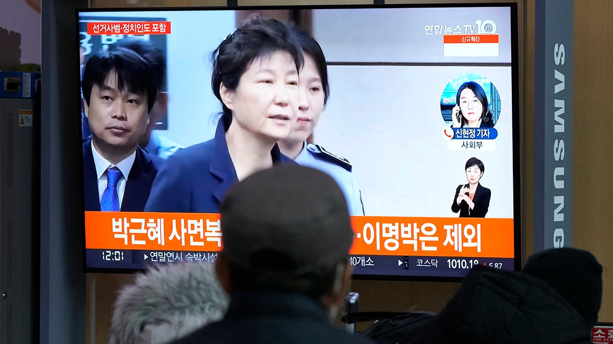 People watch a TV screen showing a file image of former South Korean President Park Geun-hye during a news program at the Seoul Railway Station in Seoul, South Korea, Friday, Dec. 24, 2021. The South Korean government said Friday it will grant a special pardon to Park, who is serving a lengthy prison term for bribery and other crimes. The Korean letters read "Pardon Park Geun-he." 