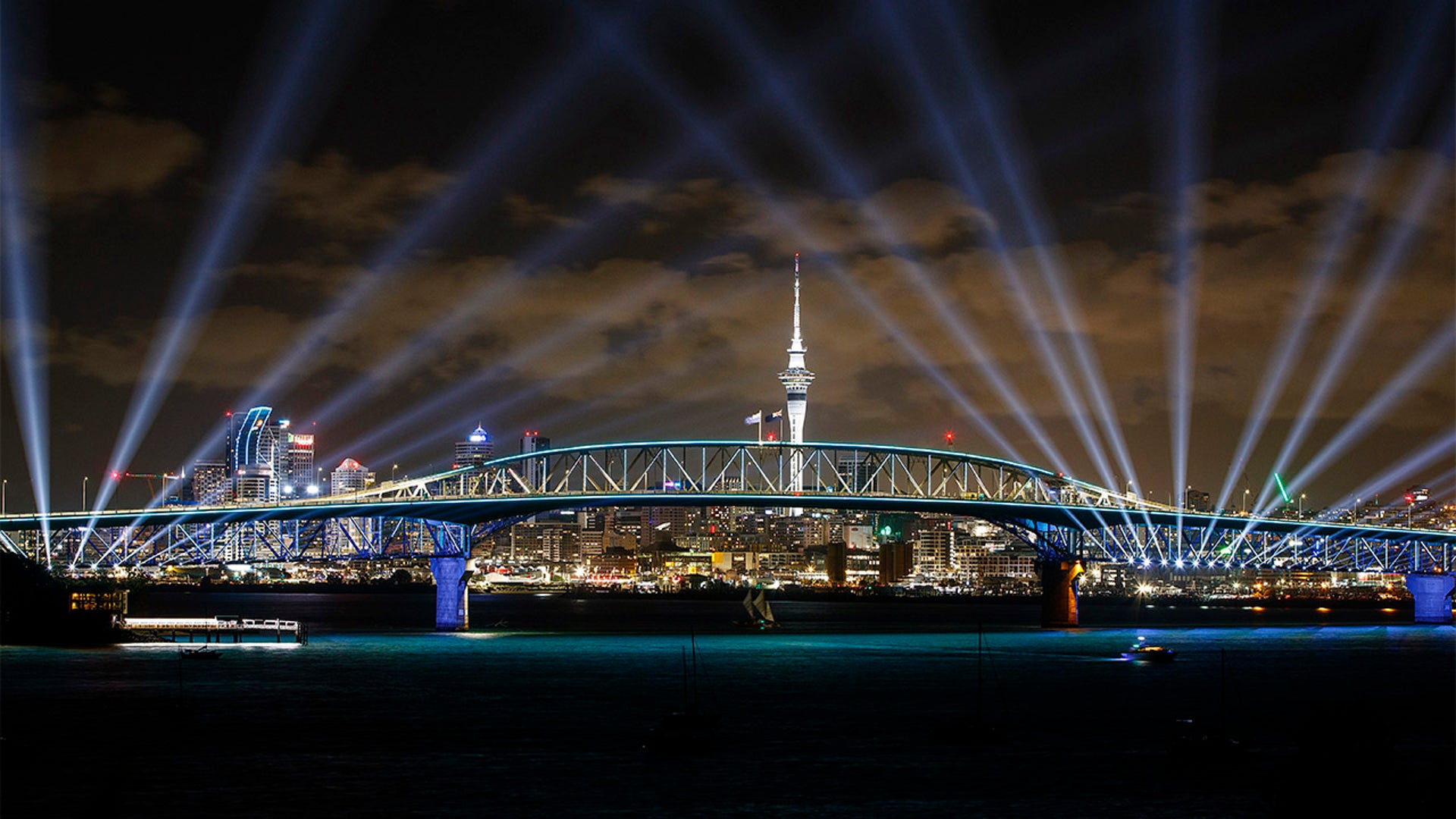 The Waka Hourua sails underneath a light show from the Skytower and harbour bridge during Auckland New Year's Eve celebrations on January 01, 2022 in Auckland, New Zealand.