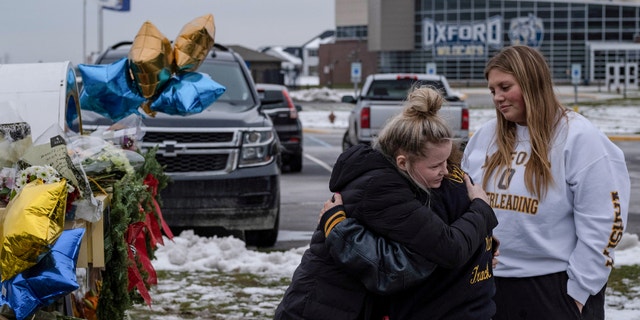People embrace as they pay their respects at a memorial at Oxford High School, a day after a shooting that left four dead and eight injured, in Oxford, Michigan. 